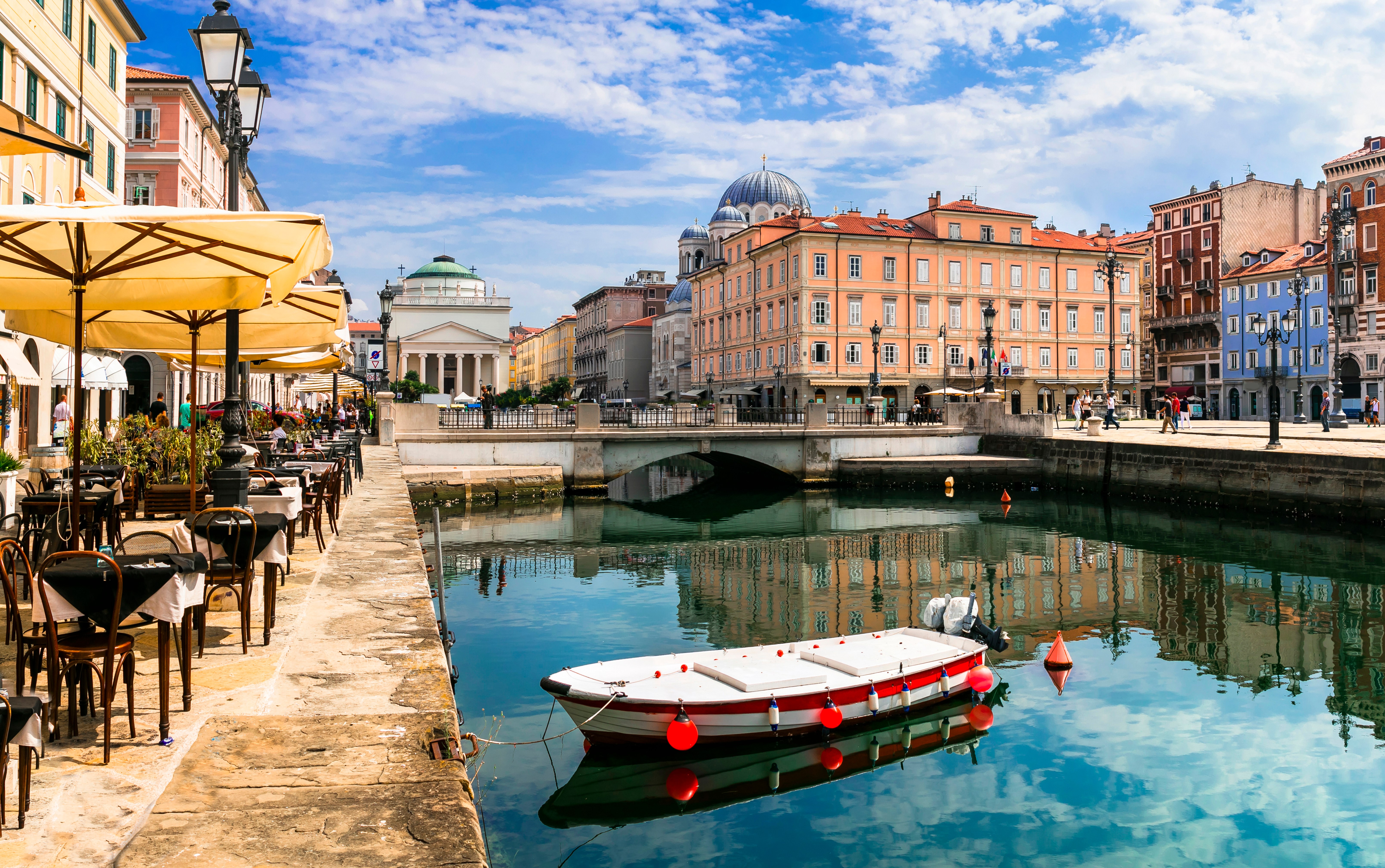 Tranquil canal in Trieste lined with restaurants and boats.