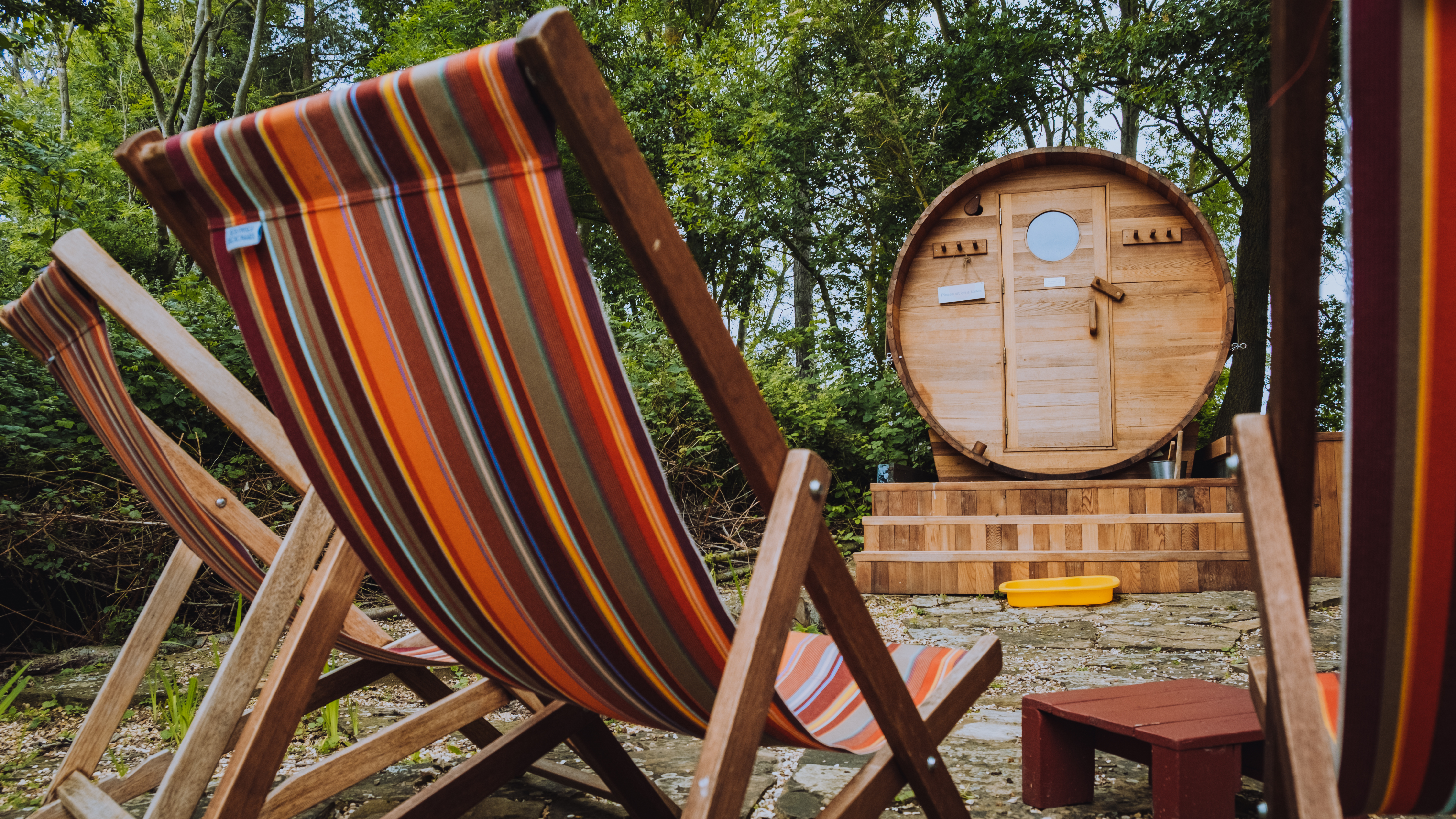 Wooden deck chairs and a barrel sauna in a wooded area.