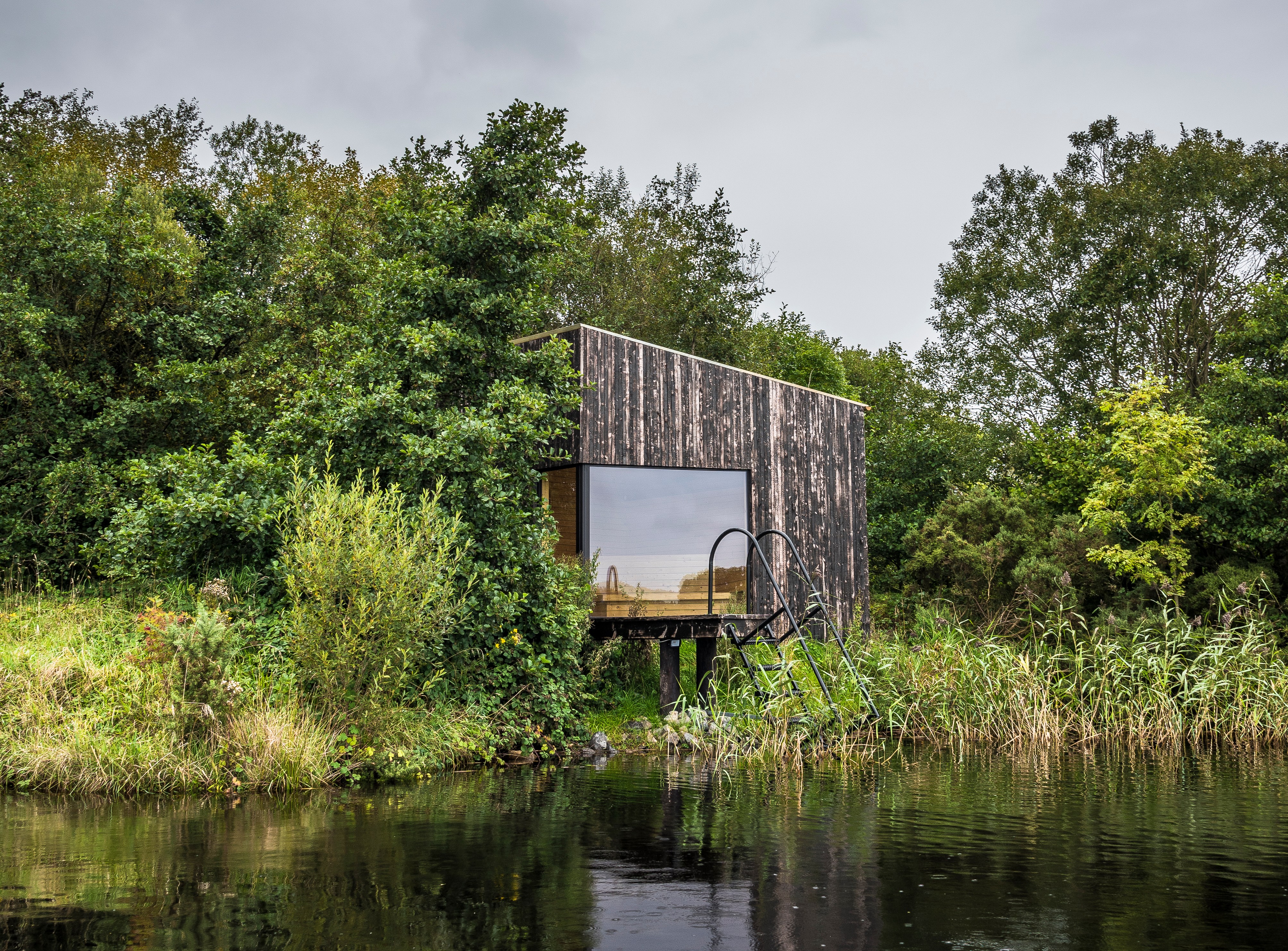 Dark wooden sauna on stilts over water.