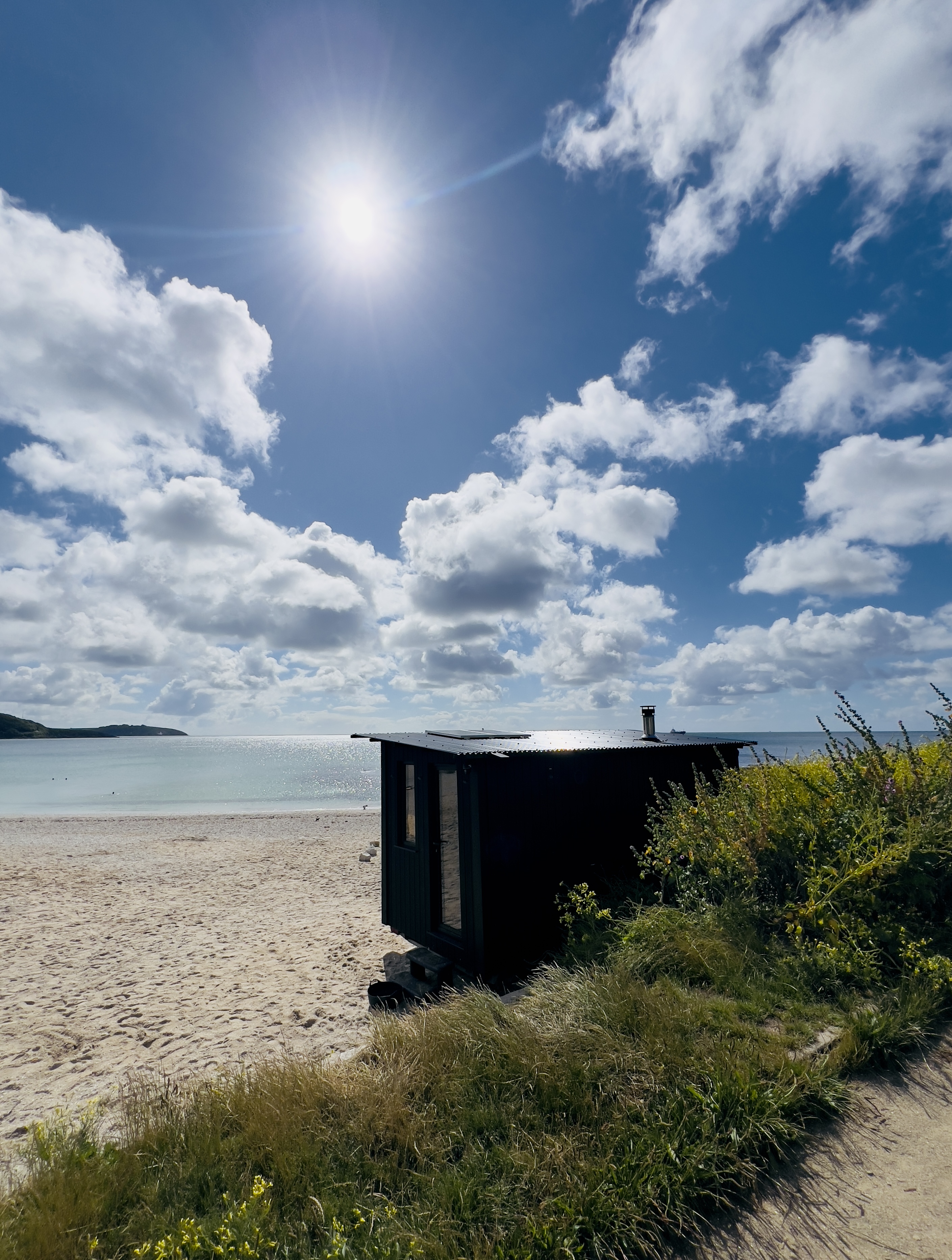 Black sauna on a sandy beach under a sunny sky.