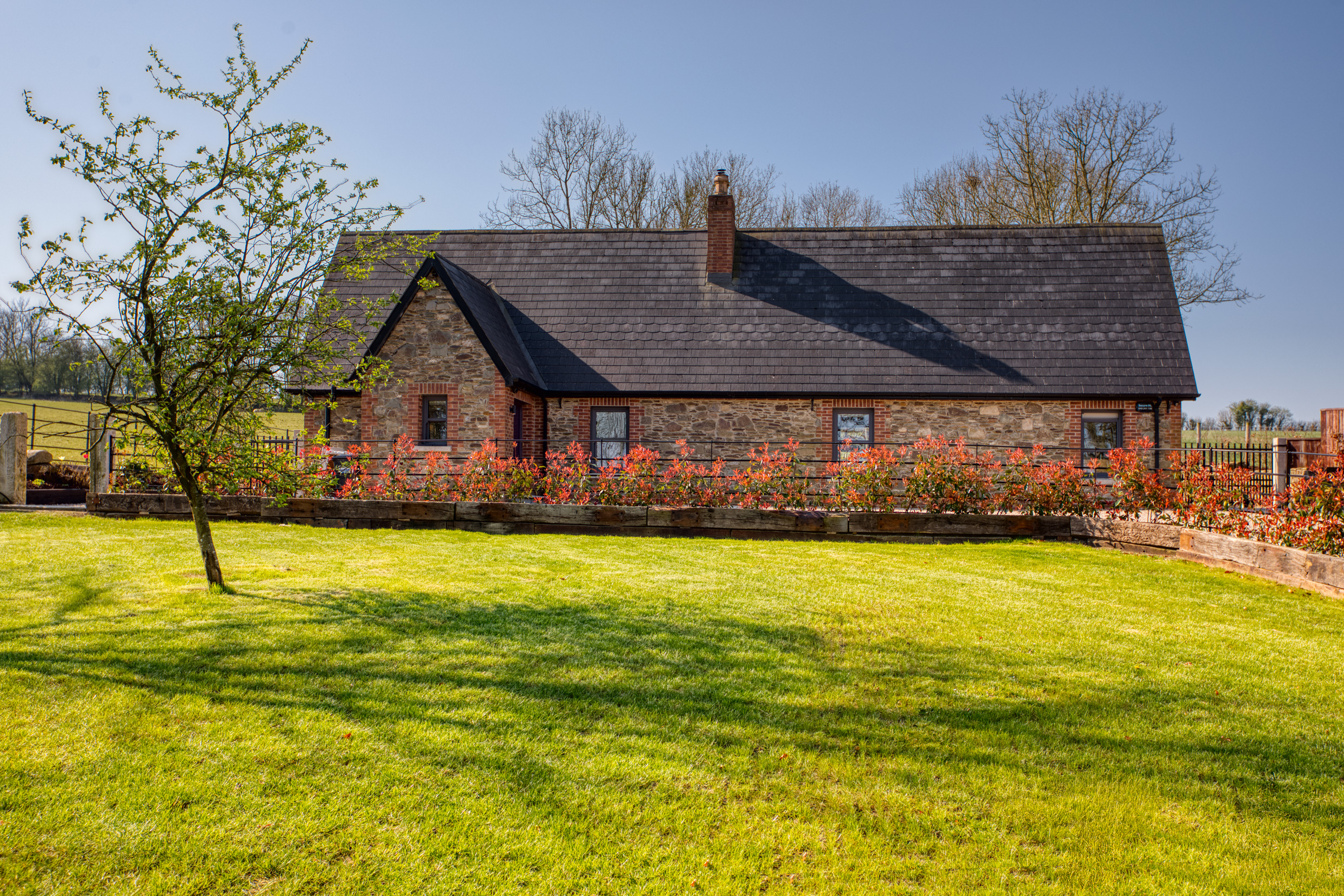 Stone cottage with a dark roof and red flowering bushes in front.