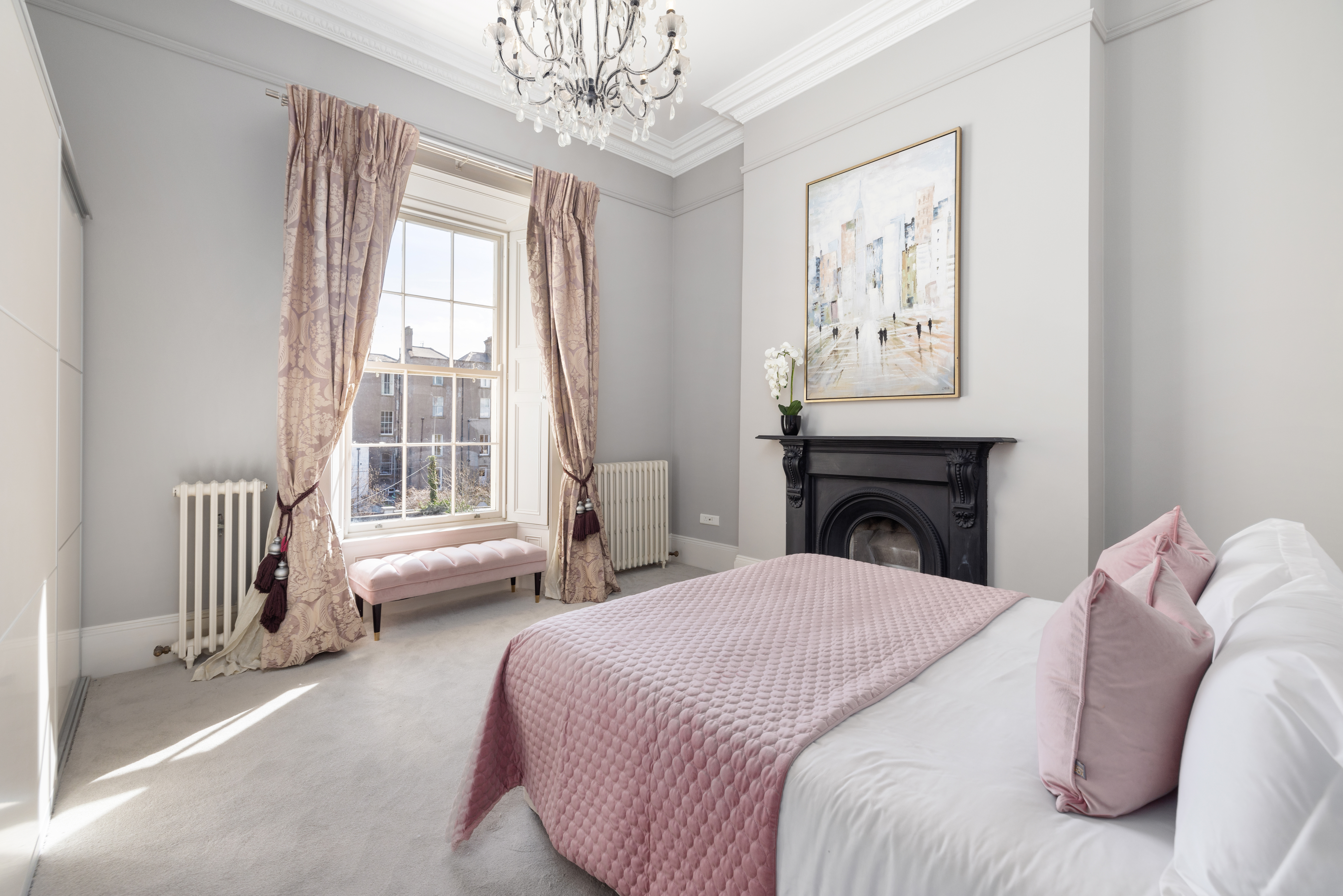 Bedroom with a large window, pink bedding, and a fireplace.