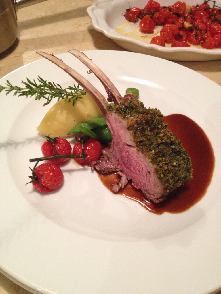 Herb-crusted rack of lamb with mashed potatoes, roasted tomatoes, and sauce.