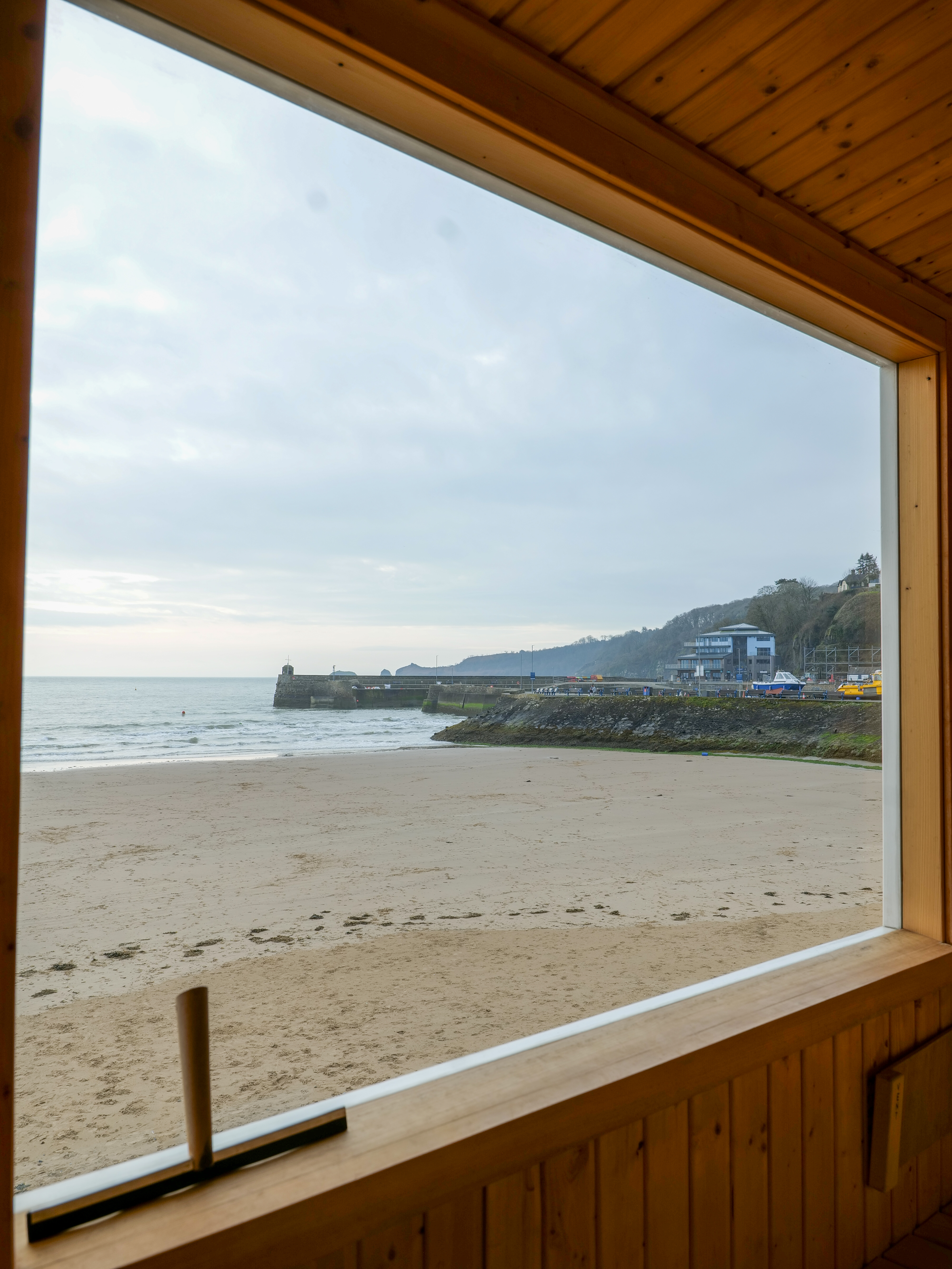 View of a beach and harbor from a wooden window.